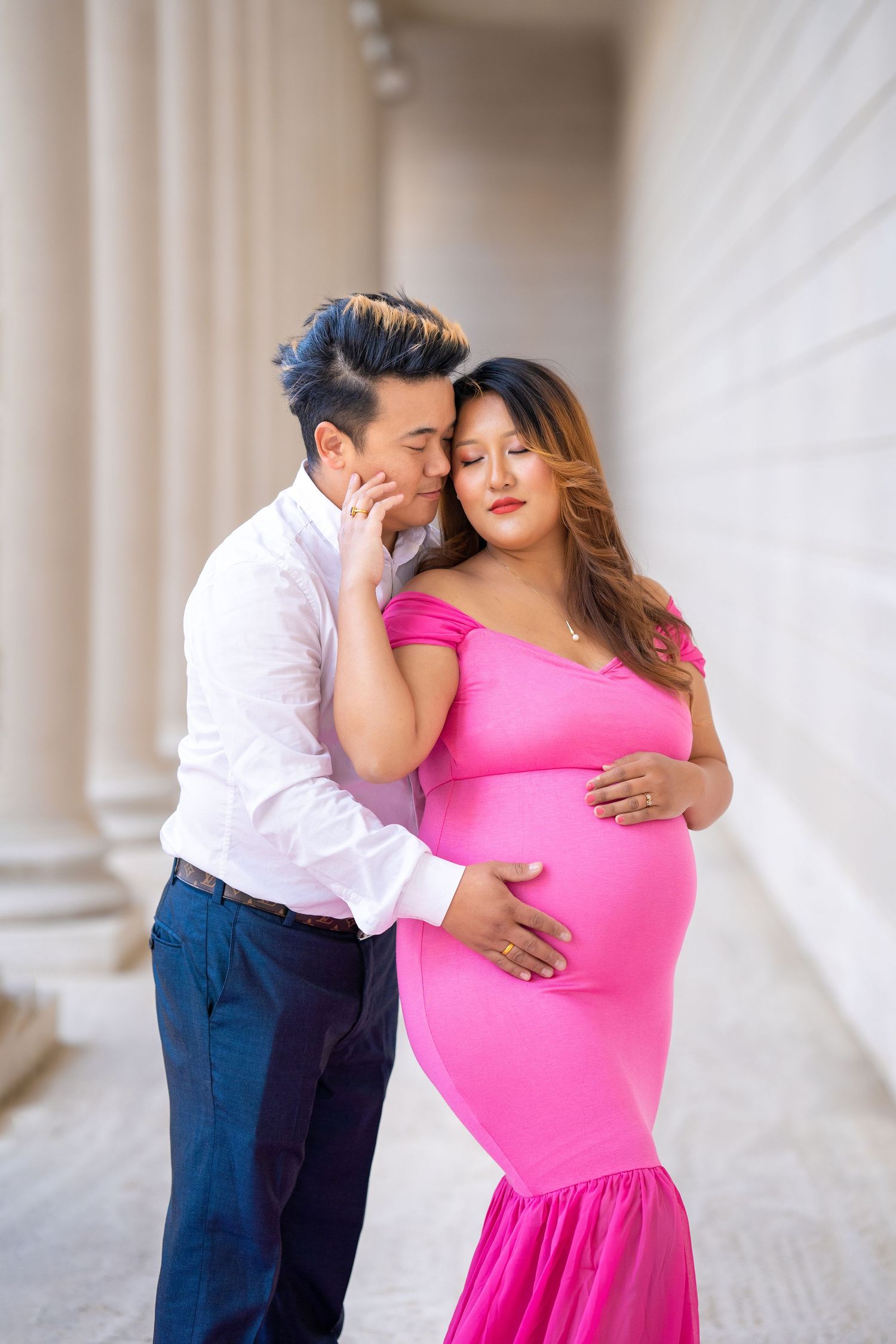 A tender maternity moment captured in a columned hallway.