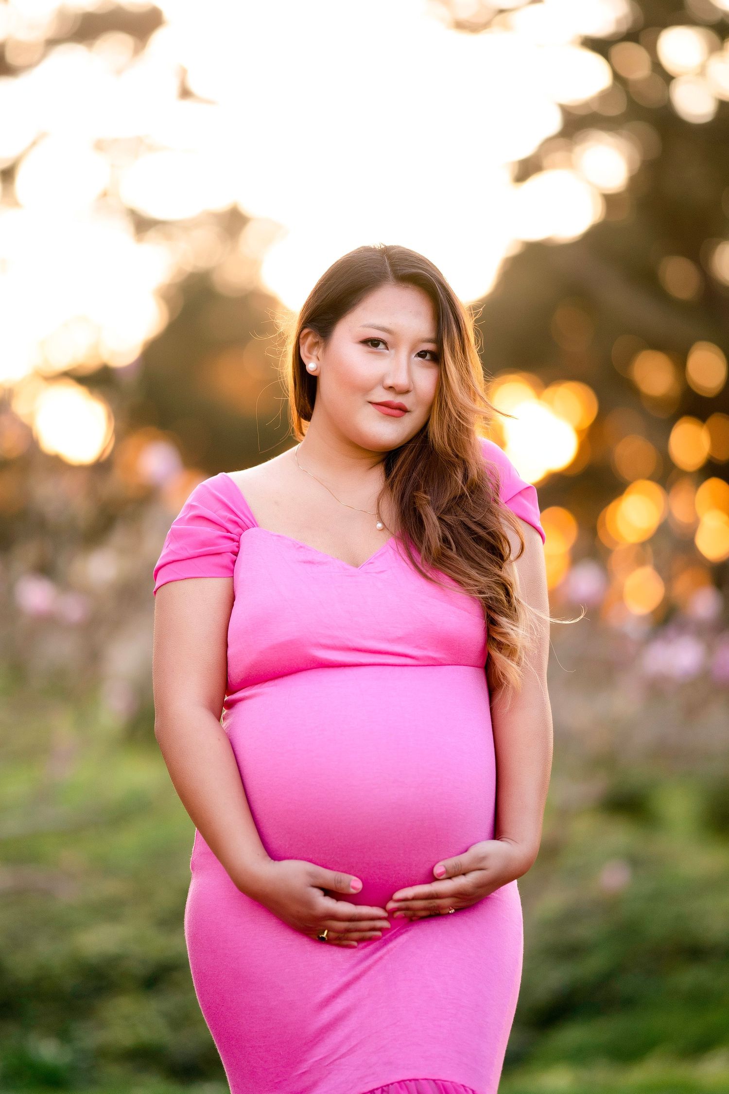 Sunset maternity photo of woman in pink dress with glowing golden background.