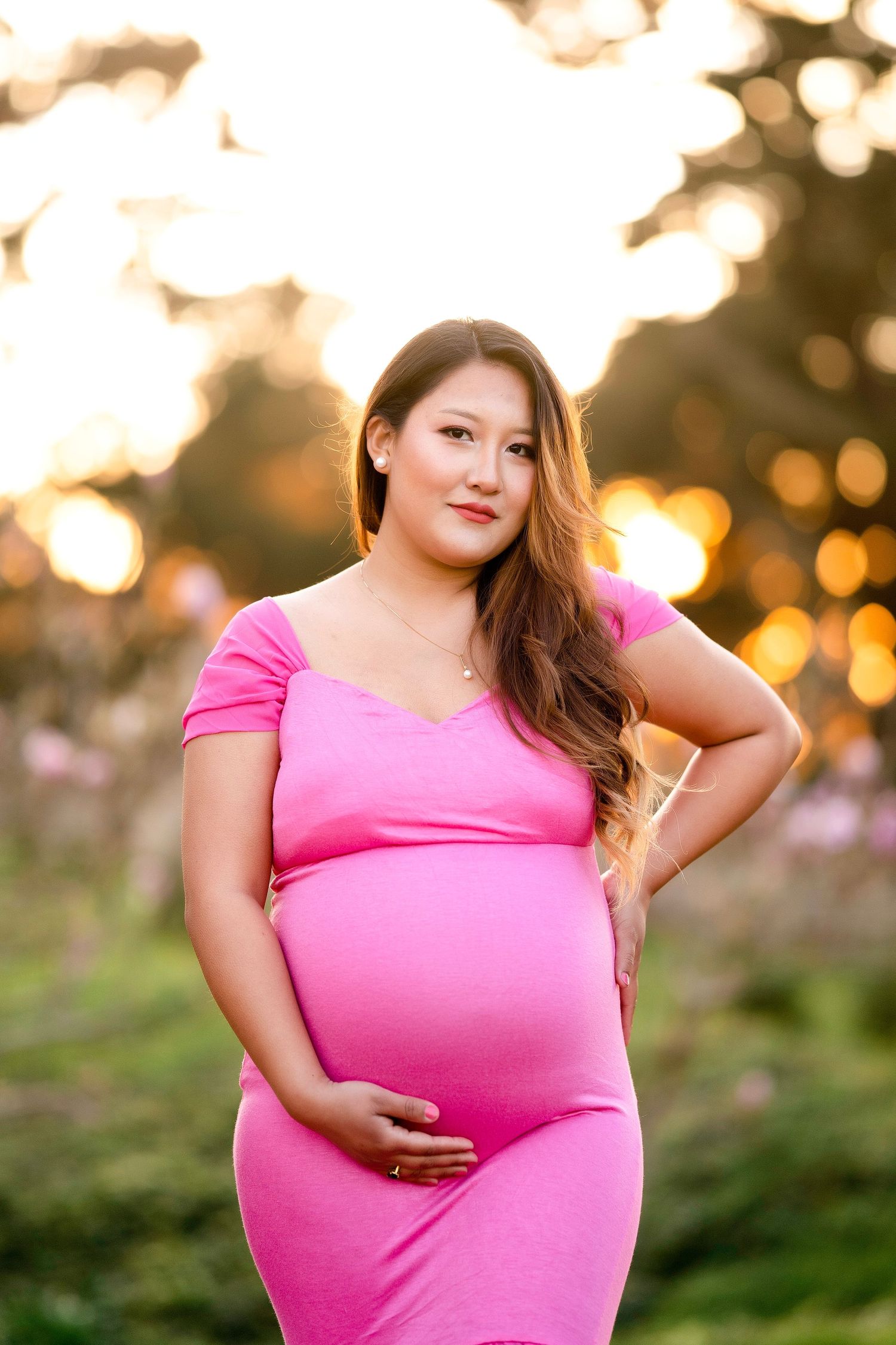 Expectant mother in pink dress poses confidently during golden hour photoshoot.
