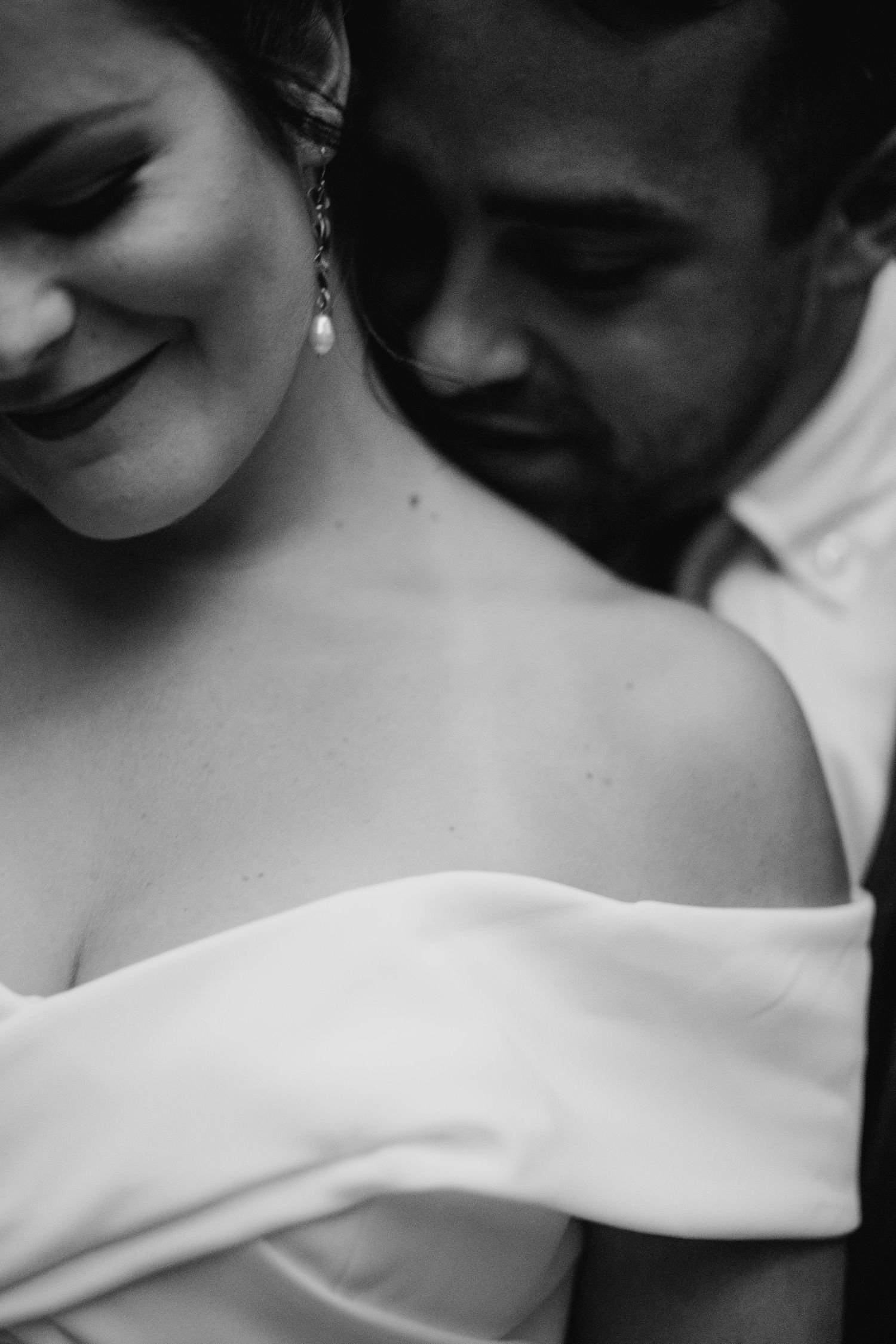 Black and white intimate close-up of a smiling bride in an off-shoulder gown with her groom nearby.