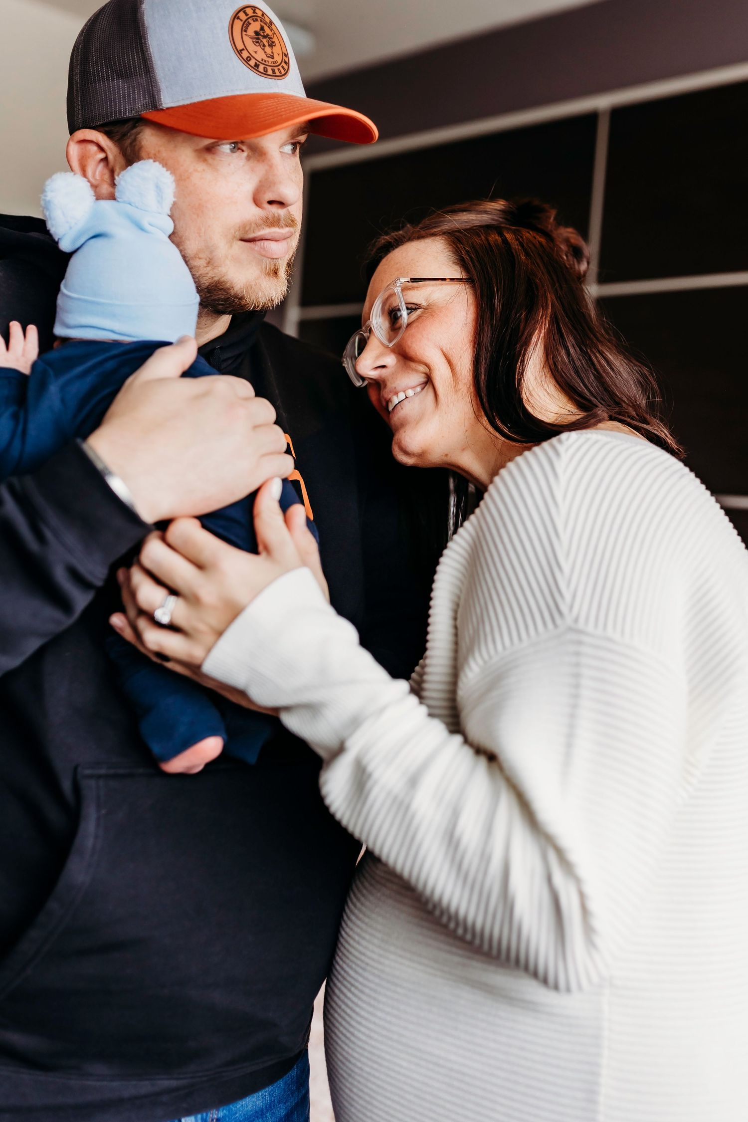 A candid family moment with parents joyfully holding their baby in a cozy indoor setting.
