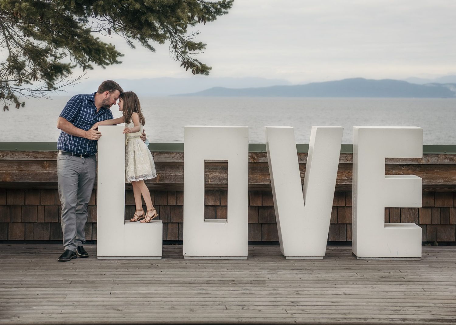 Couple posing with large white LOVE letters on outdoor deck with mountain vista.