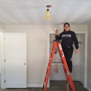 Person standing on orange ladder in empty white room during renovation.