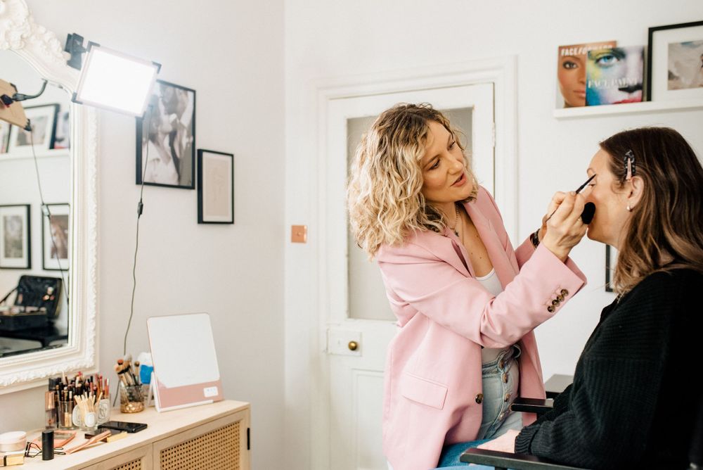 Professional makeup application in progress at a beauty studio with soft natural lighting.