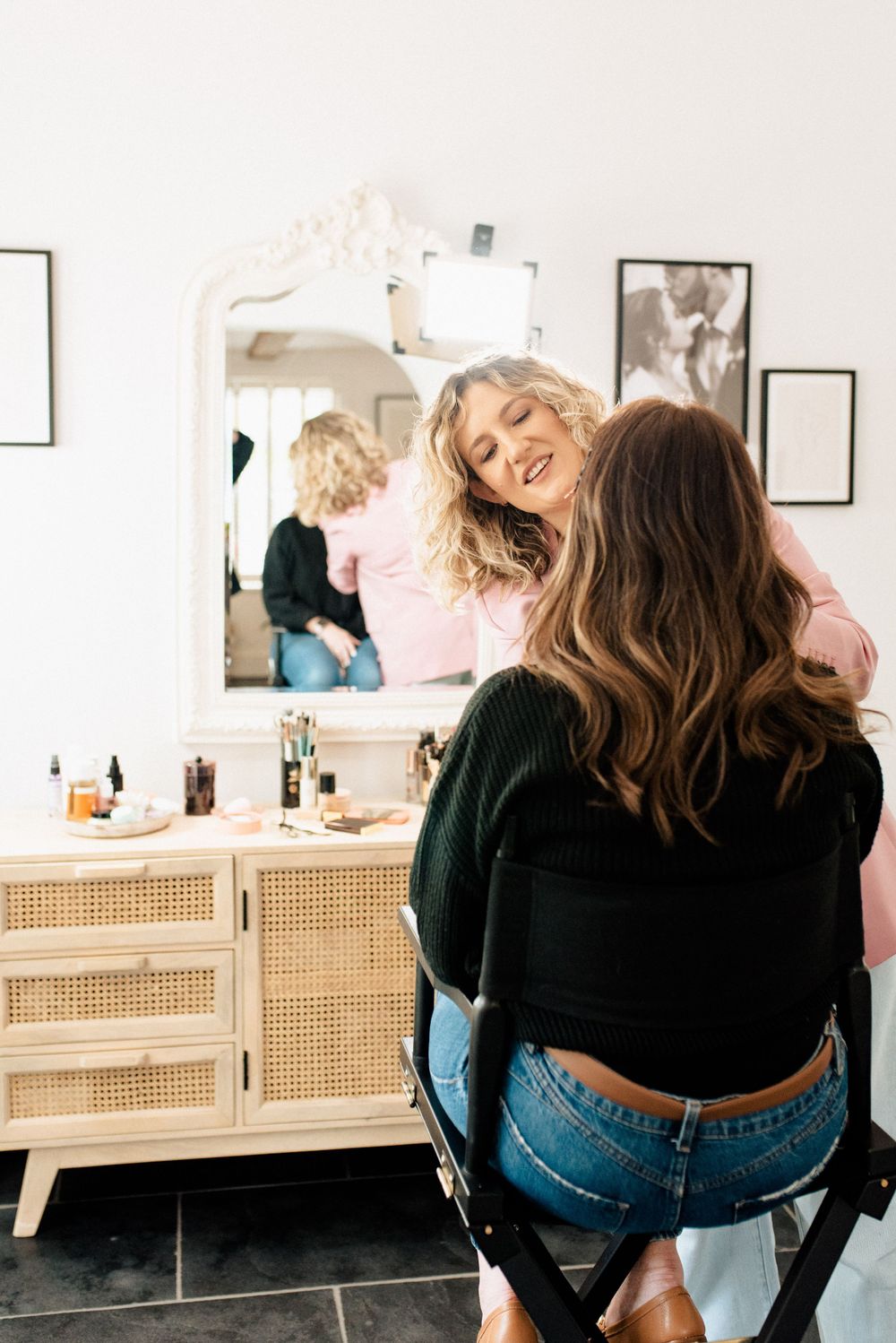 Professional makeup artist working with client in front of vanity mirror with cane cabinet storage.
