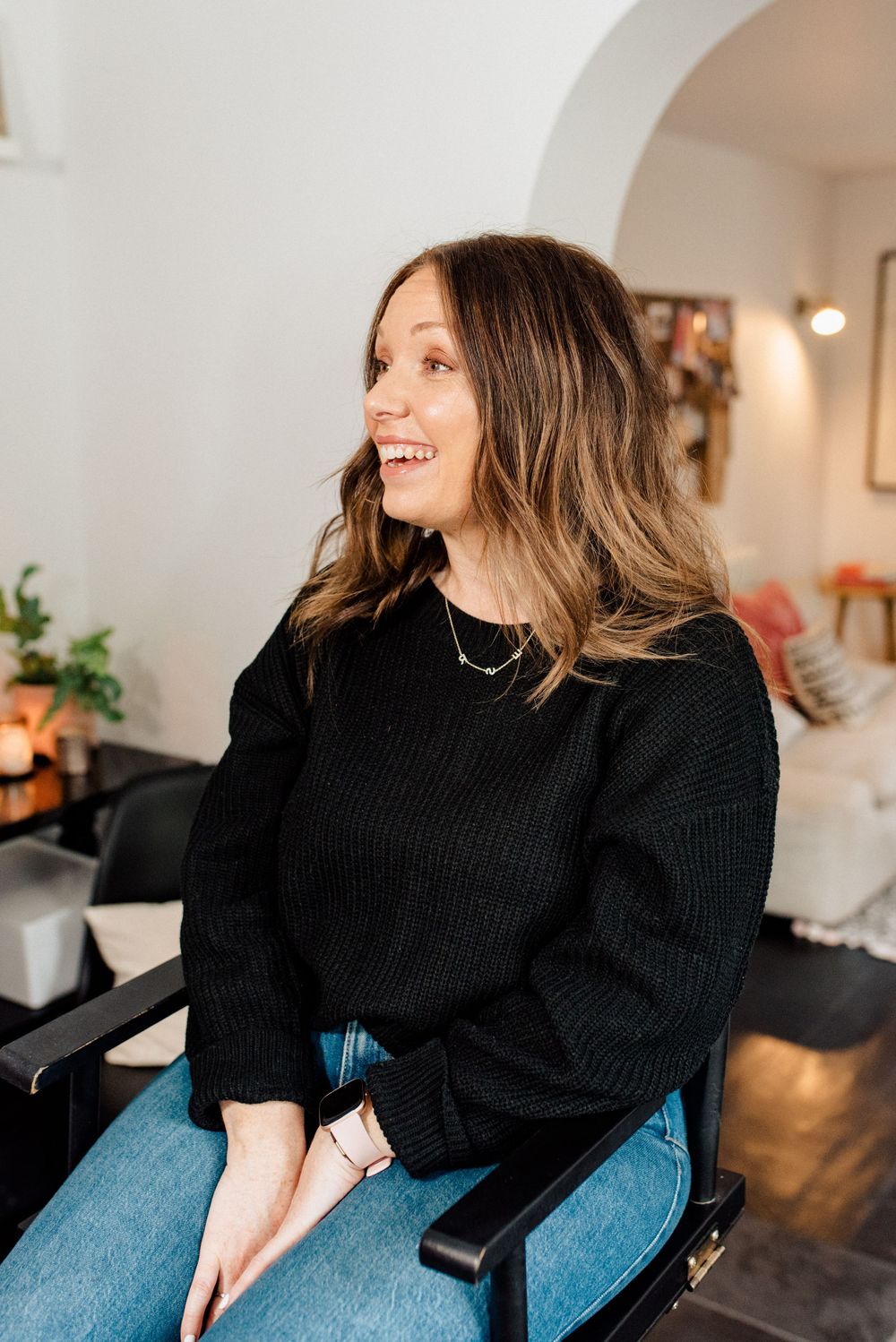 Client in black sweater smiles while seated in makeup chair during beauty session.