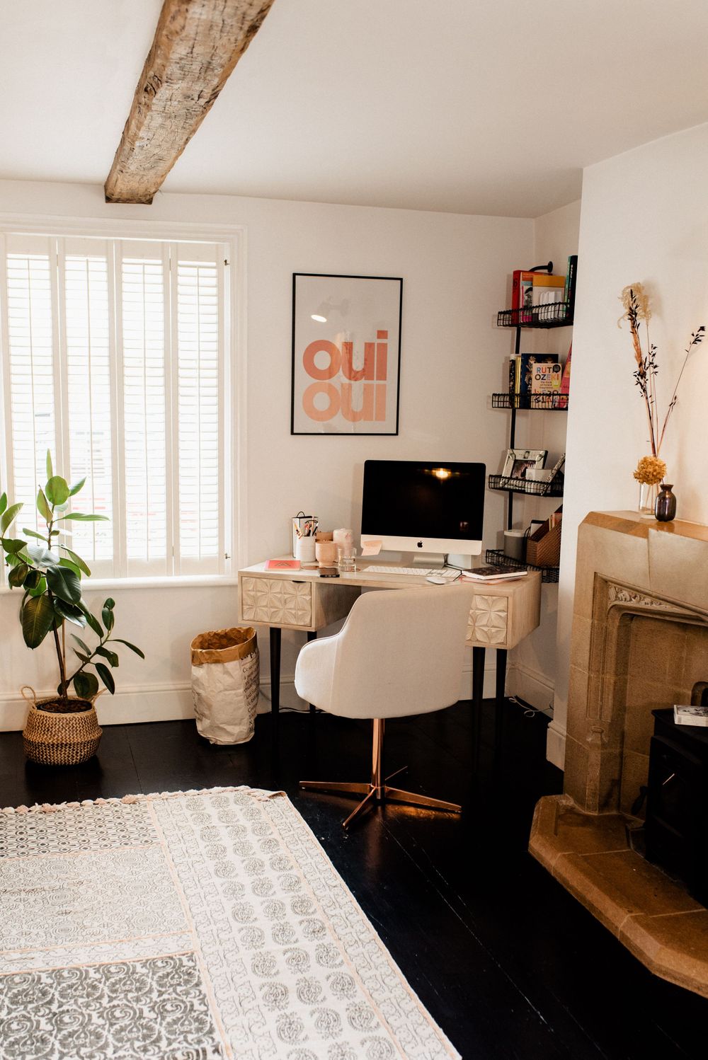 Modern home office with white walls, wooden beam, and pink accents featuring 'Oui Oui' artwork.