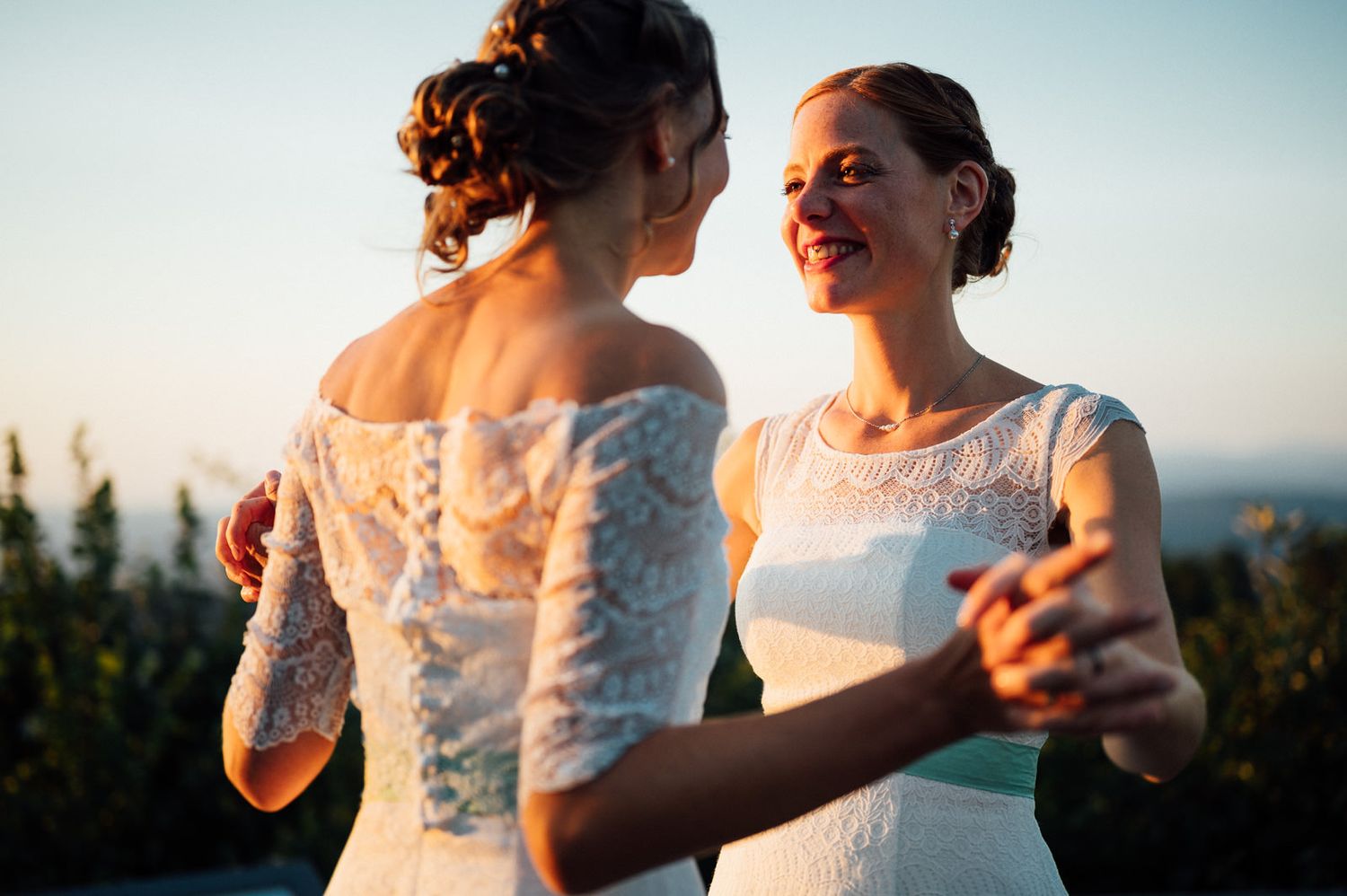 Two people in white lace dresses dance together in warm sunset light.