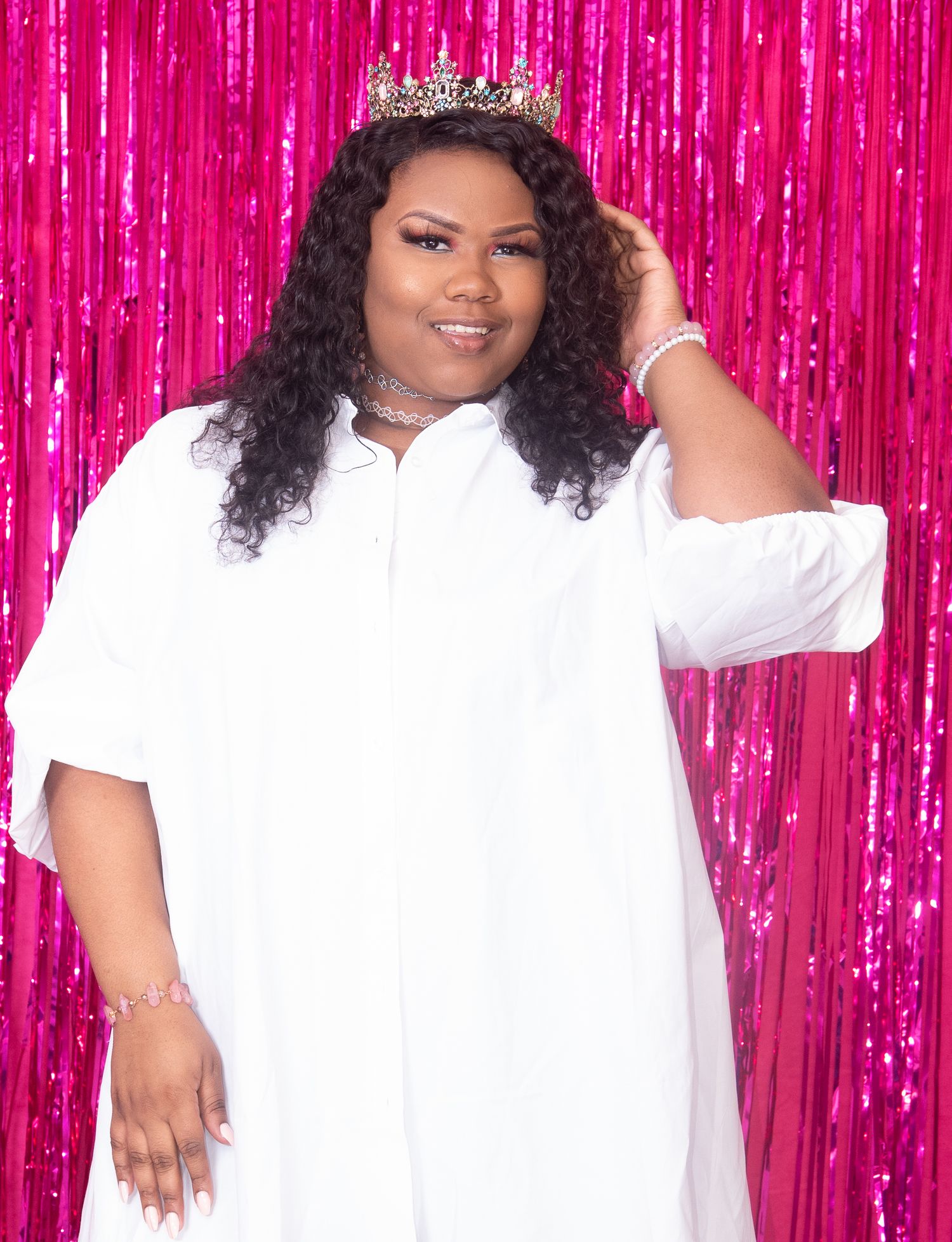 Portrait against pink backdrop wearing white outfit and sparkling crown.