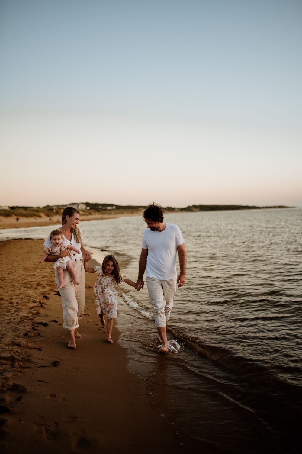 Familj går på stranden längs havet i solnedgången. Golden hour.