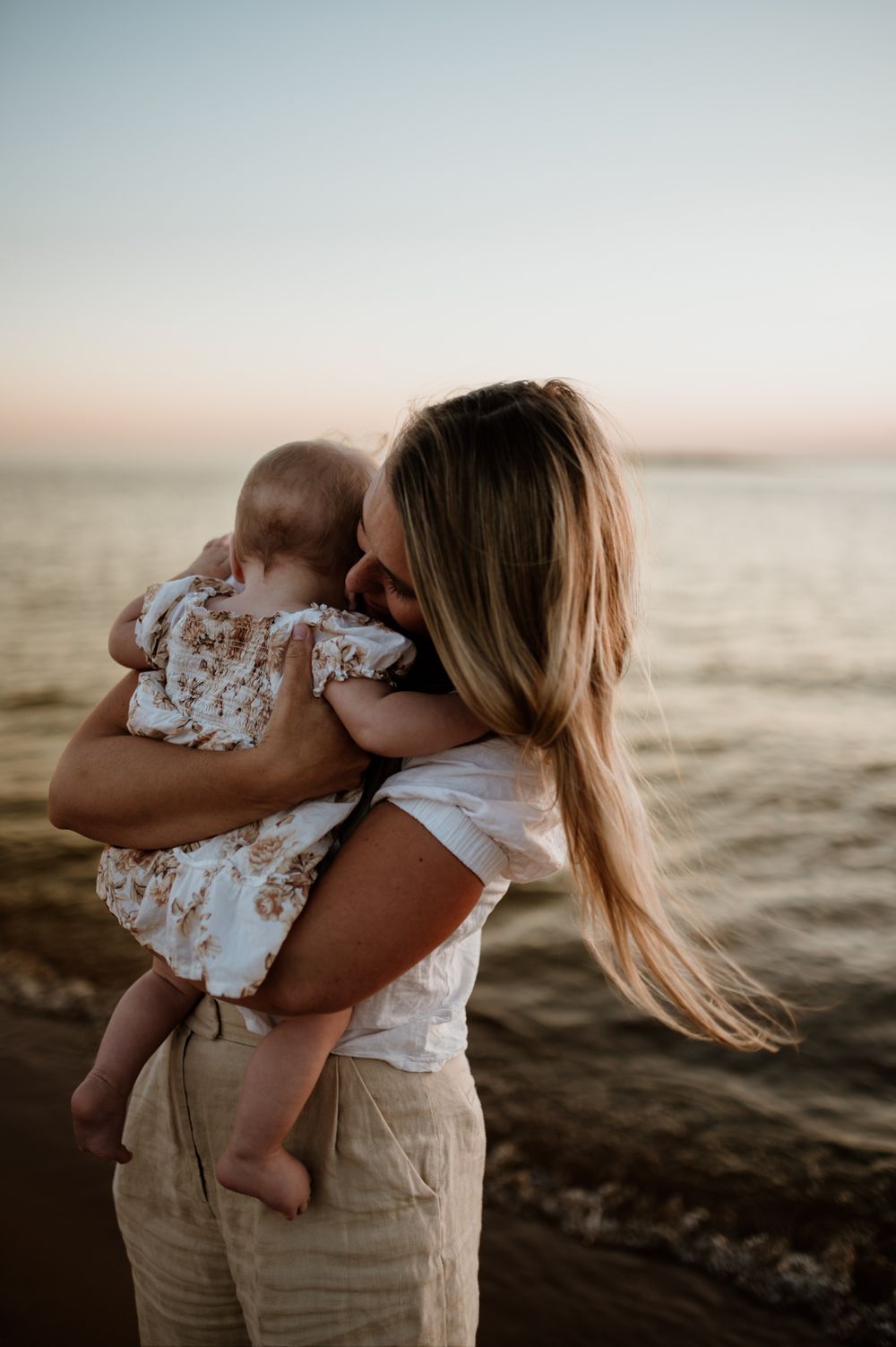 Mamma och dotter vid havet i solnedgången. Golden hour.