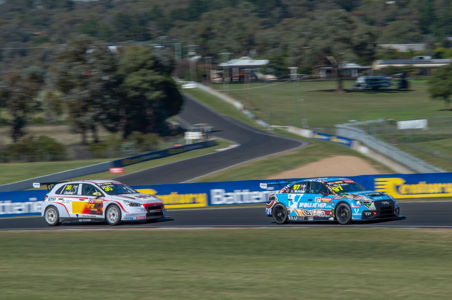 Two touring cars racing side by side on professional race circuit.