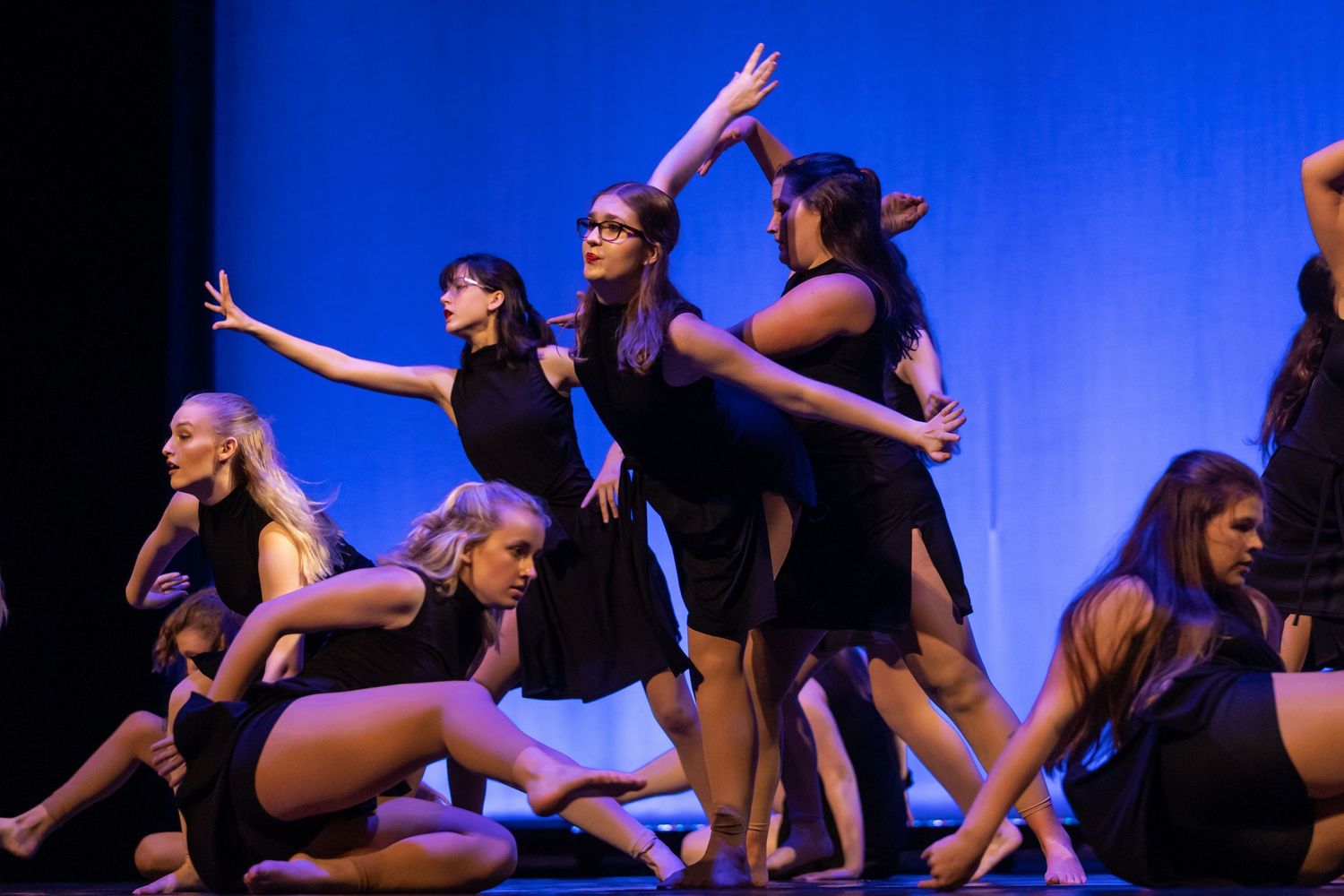 Silhouettes of dancers performing on stage against vibrant blue lighting.