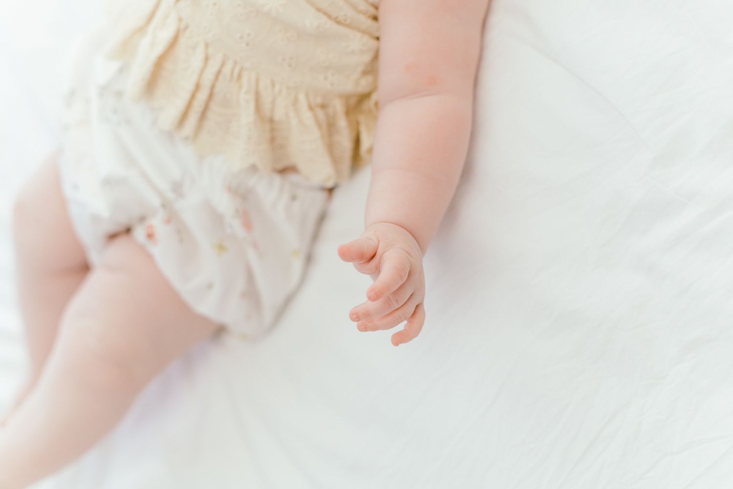 Close-up of tiny baby hand against white bedding.