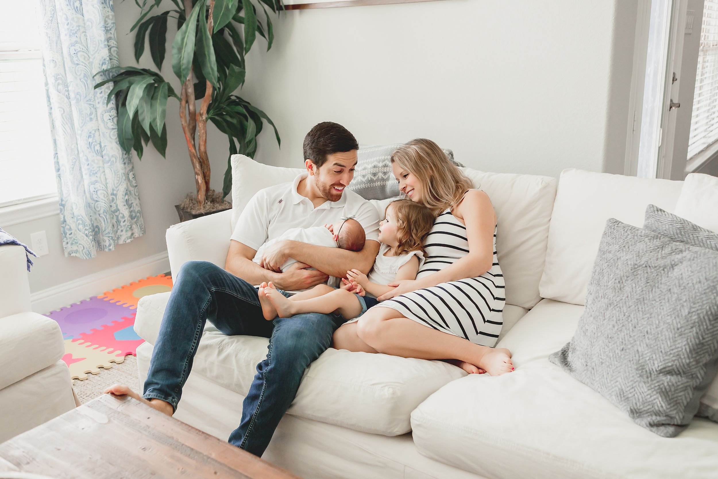 A family casually sits on couch looking at the new member of the family in a lifestyle session in Houston, TX.