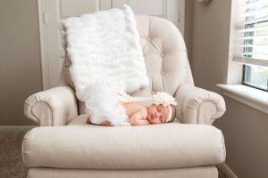 Baby girl with angel wings asleep on a white chair near a window for her newborn session in Houston, TX.