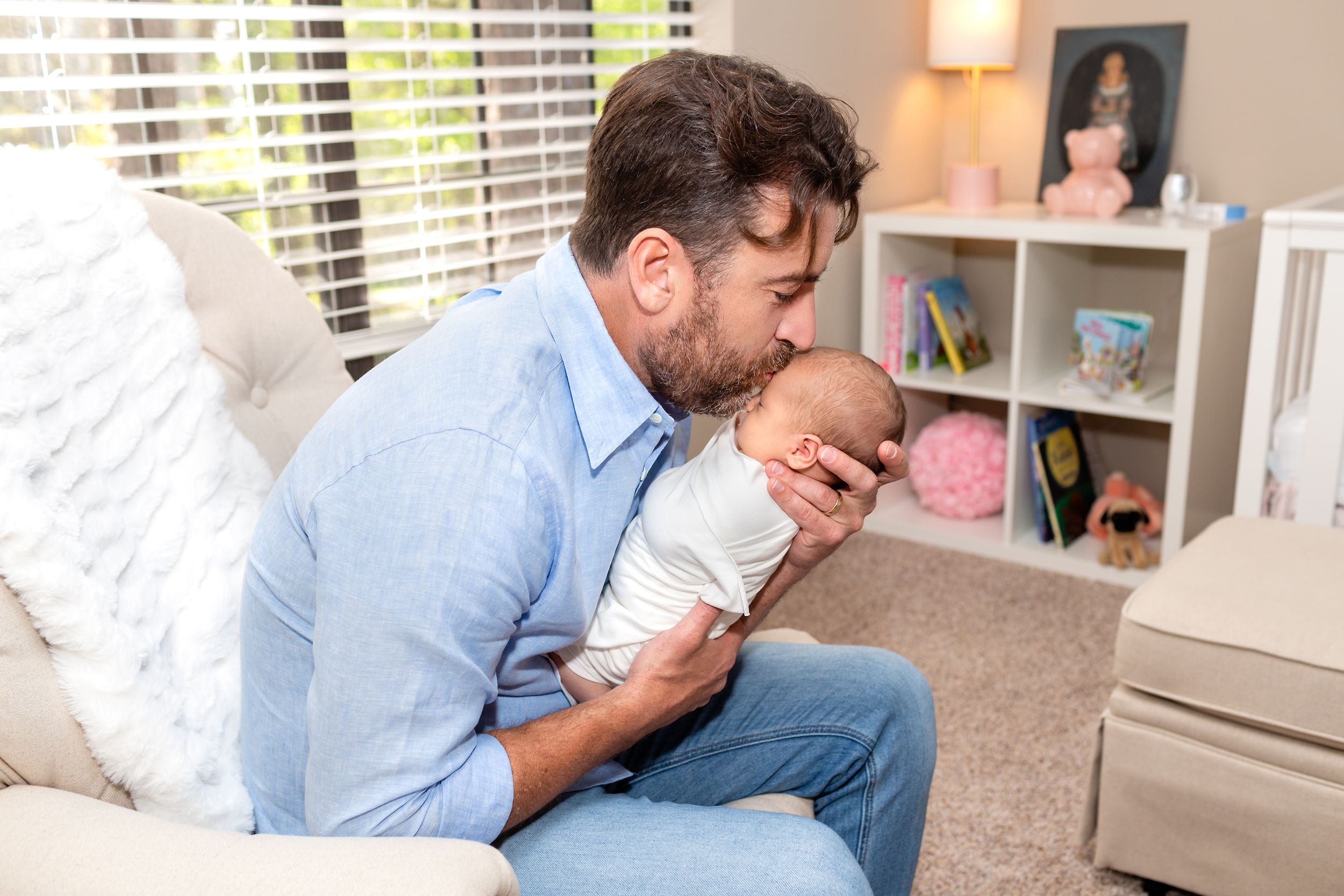 Dad kisses baby girl on the forehead while holding her in her nursey for their newborn session.