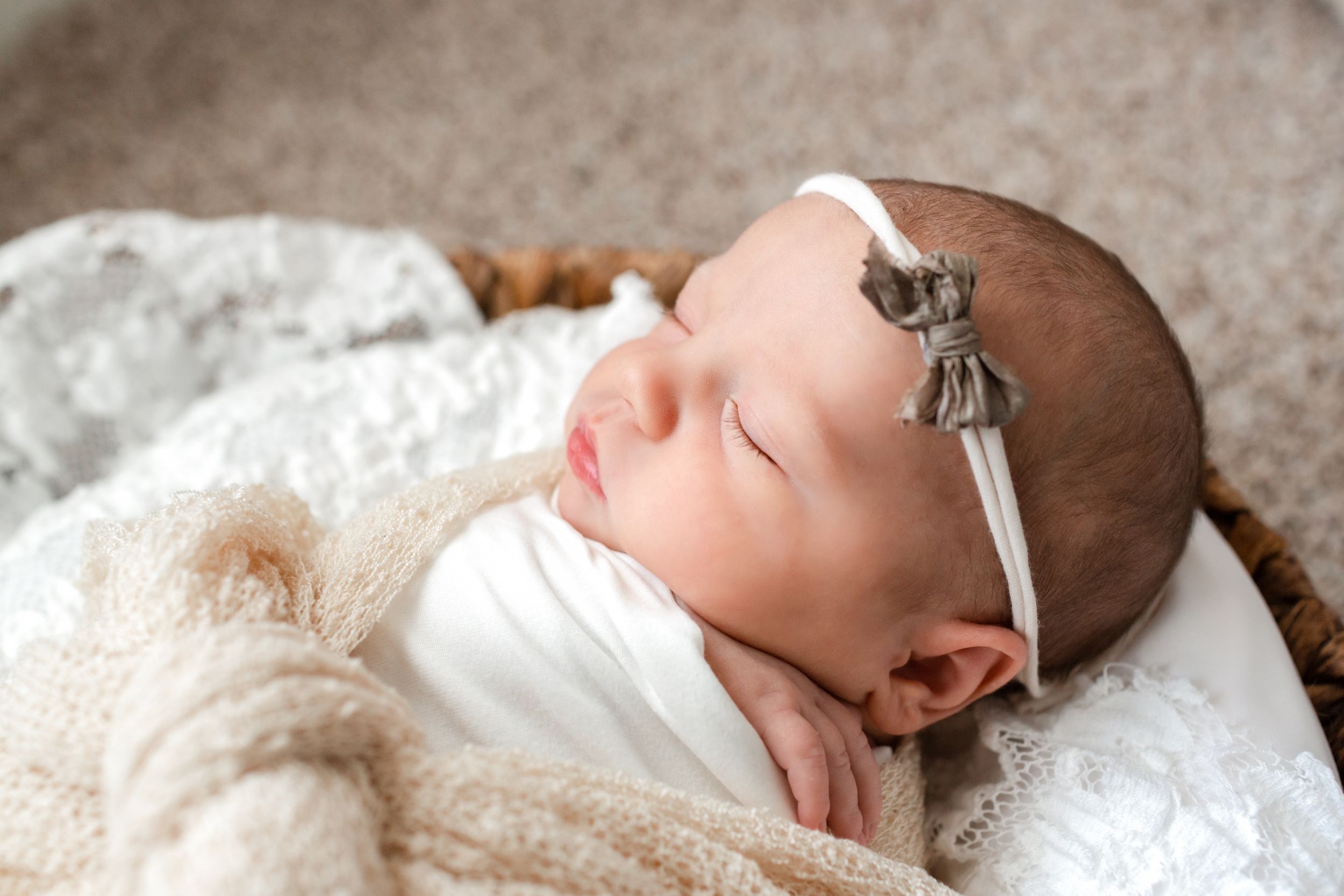 Baby girl asleep in a basket wrapped in white and cream for her newborn session in Houston, TX.