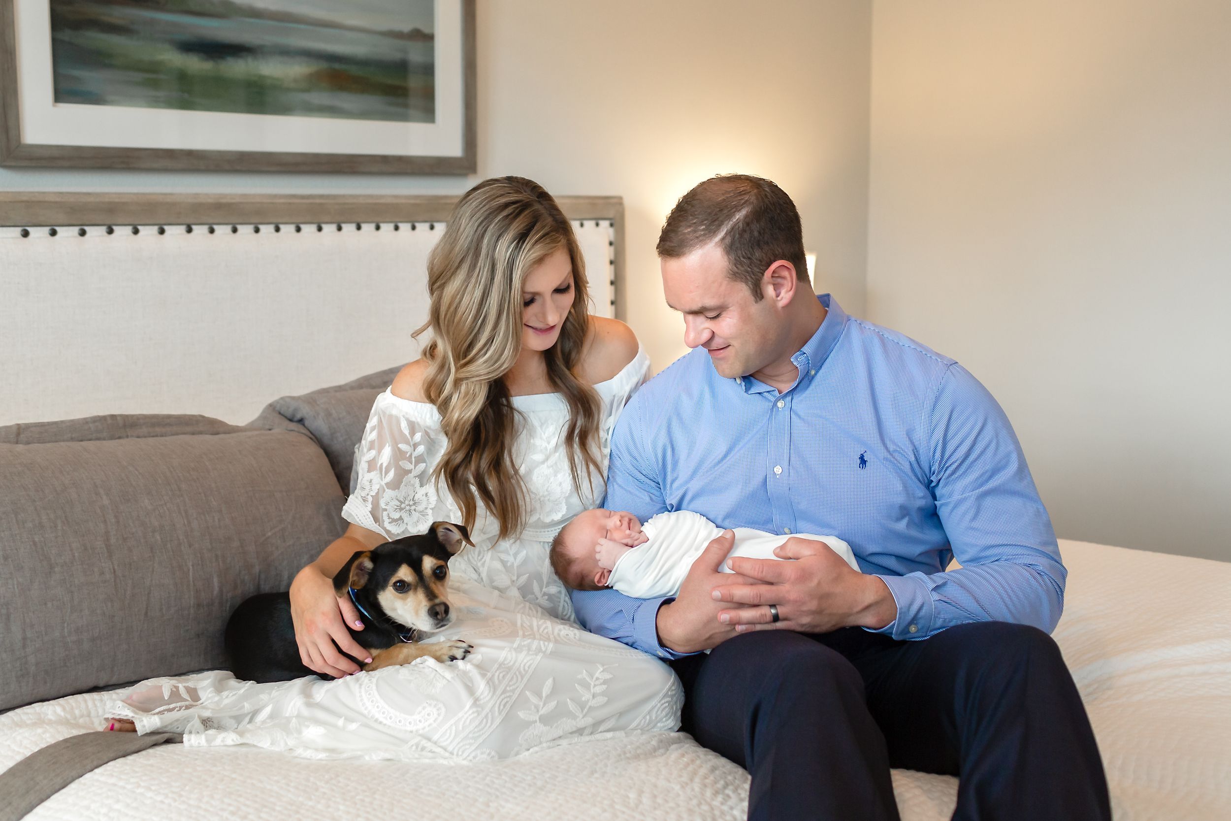Couple with dog looks at their new baby boy while casually sitting on their bed in their home in Houston, TX.