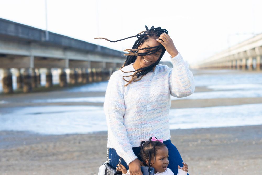 Parent and child at waterfront location with long dreadlocks flowing in wind.