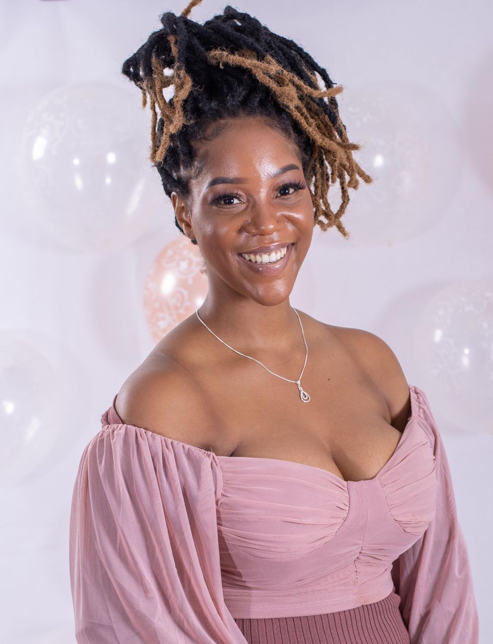 Studio portrait with pink balloons and person wearing off-shoulder dress.
