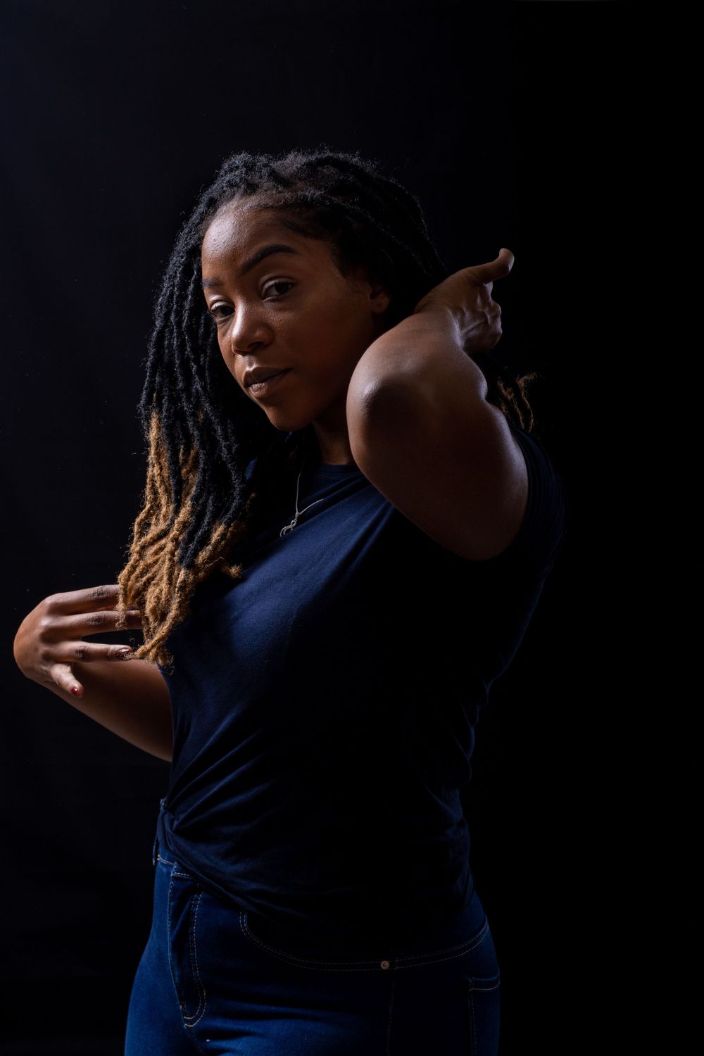 Dramatic studio portrait against black background showing dynamic pose in navy blue outfit.