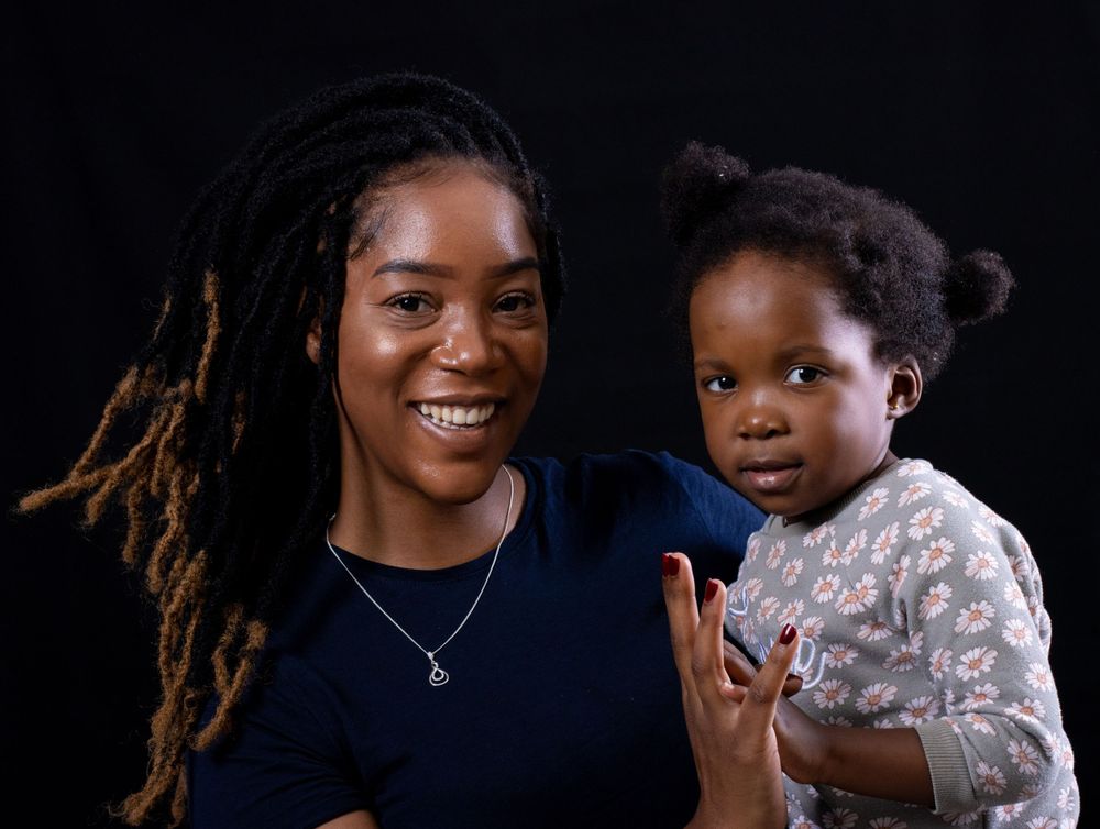 Parent and child share joyful moment during studio photoshoot against black backdrop.