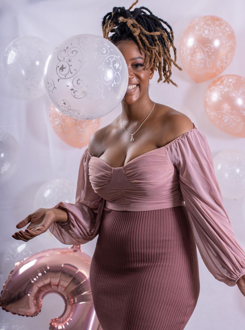Person in pink dress poses with balloons at celebration event.