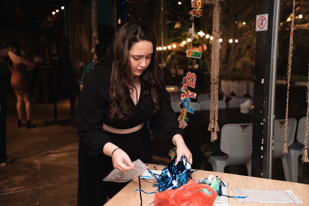 Person arranging items on a table at a nighttime outdoor event with string lights.