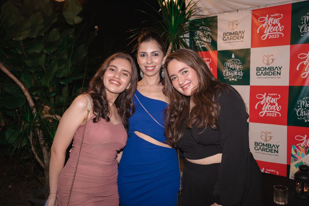 Three friends pose together at an event with branded step-and-repeat backdrop.