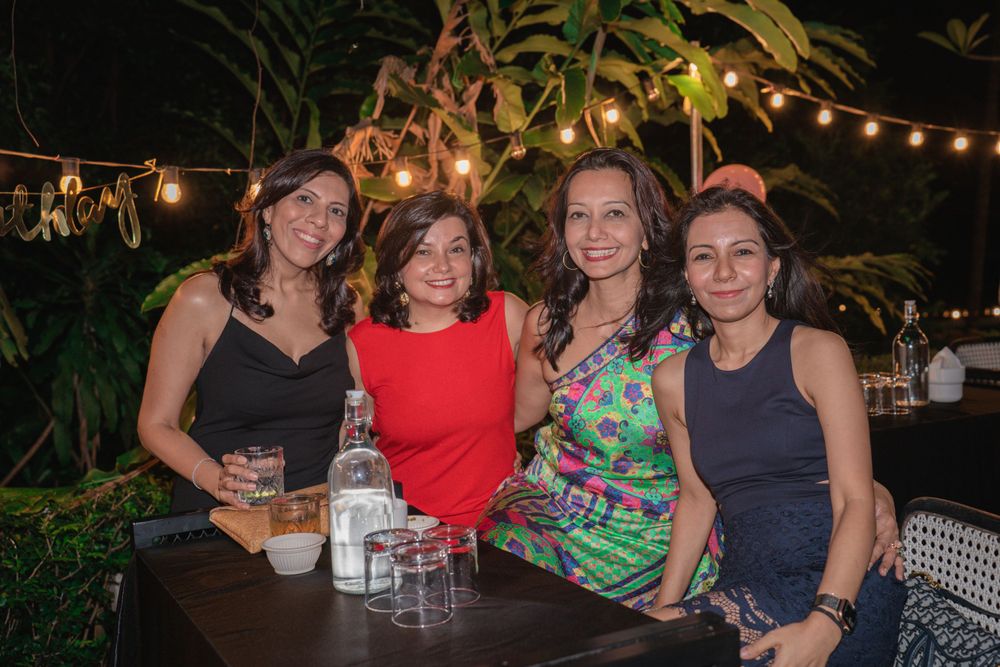 Group enjoying drinks and conversation at an outdoor patio with string lights and tropical plants.