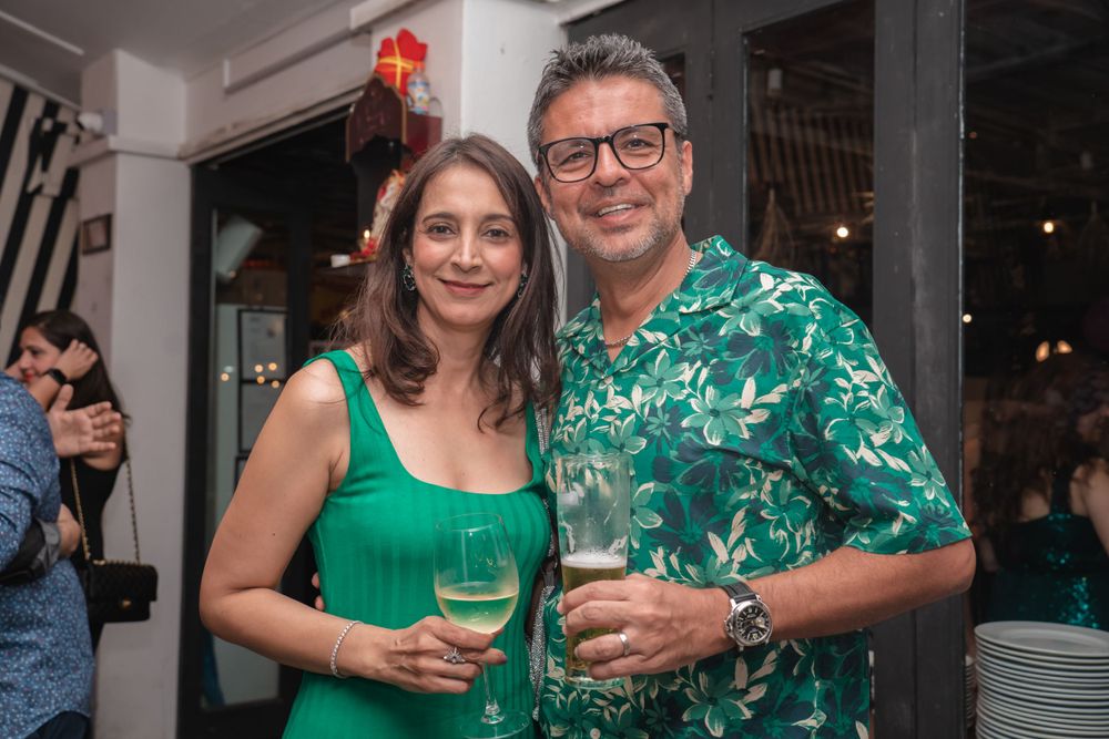 Couple in coordinating green outfits holding drinks at an indoor party.