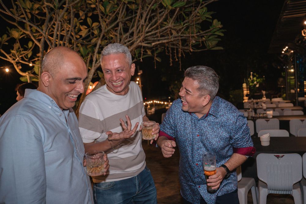 Three friends sharing drinks and laughs during outdoor evening celebration.