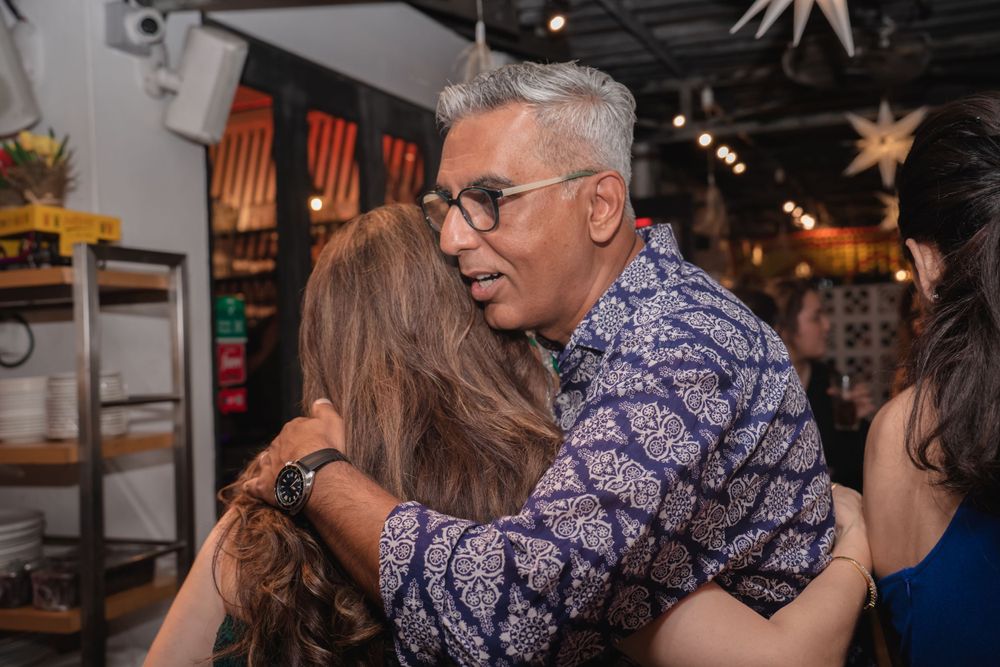 Two people sharing an emotional embrace at an indoor event with decorative lighting.