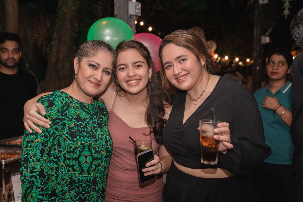 Friends posing together at a nighttime gathering with drinks and string lights.