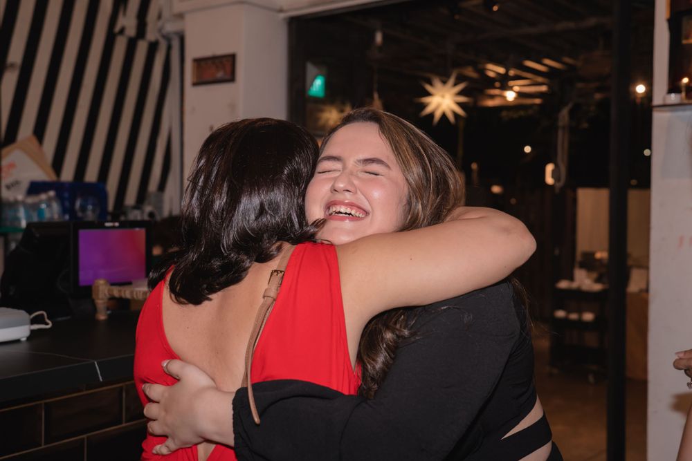 Two people sharing a joyful embrace in front of striped wall decor at an indoor venue.