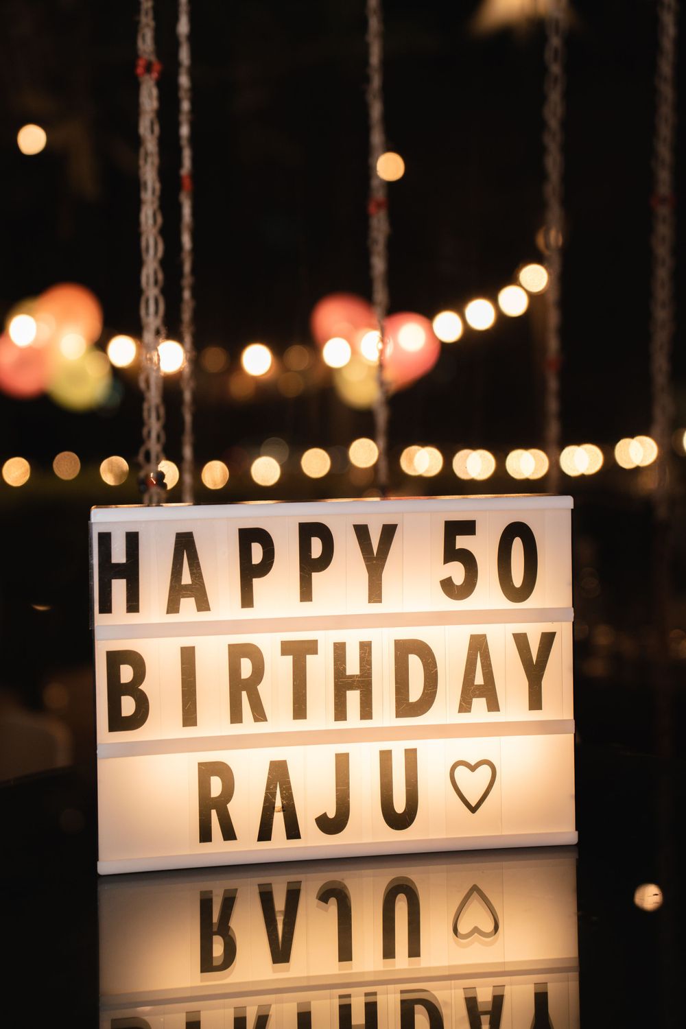 Illuminated lightbox displaying Happy 50th Birthday Raju message against string lights.