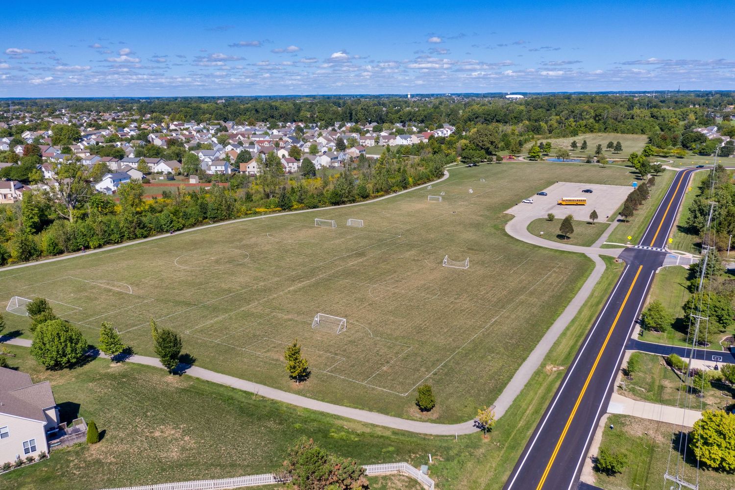 Aerial view of an open green field with soccer goals next to a residential neighborhood and paved road.
