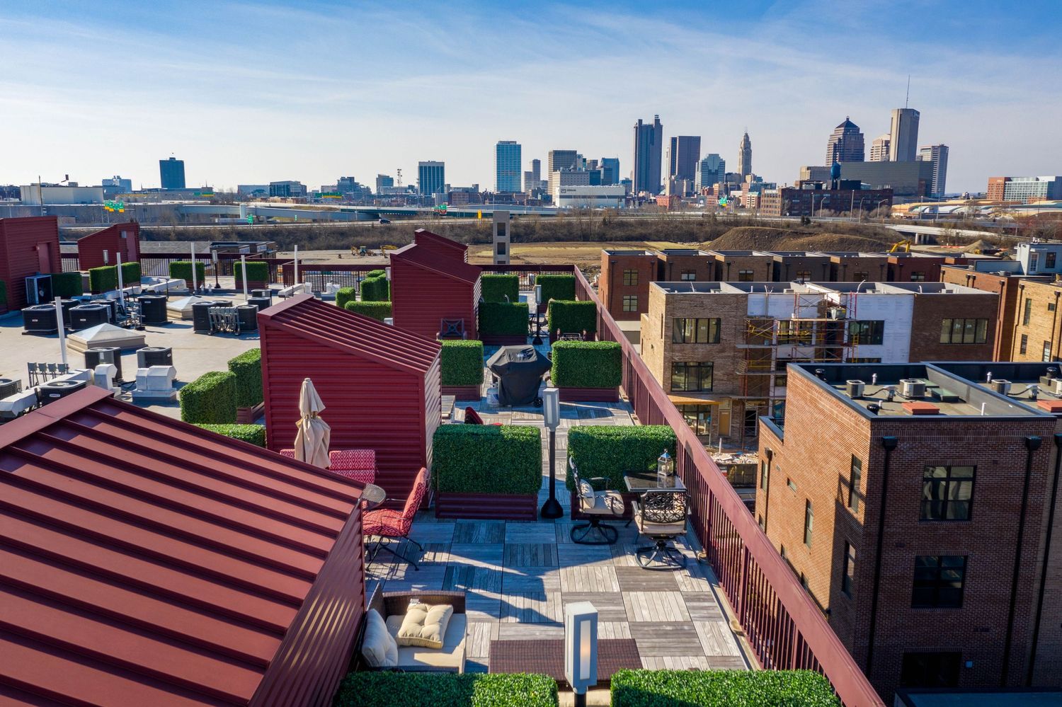 Aerial view of downtown Columbus Ohio skyline with colorful urban rooftops and buildings in the foreground beneath blue sky.
