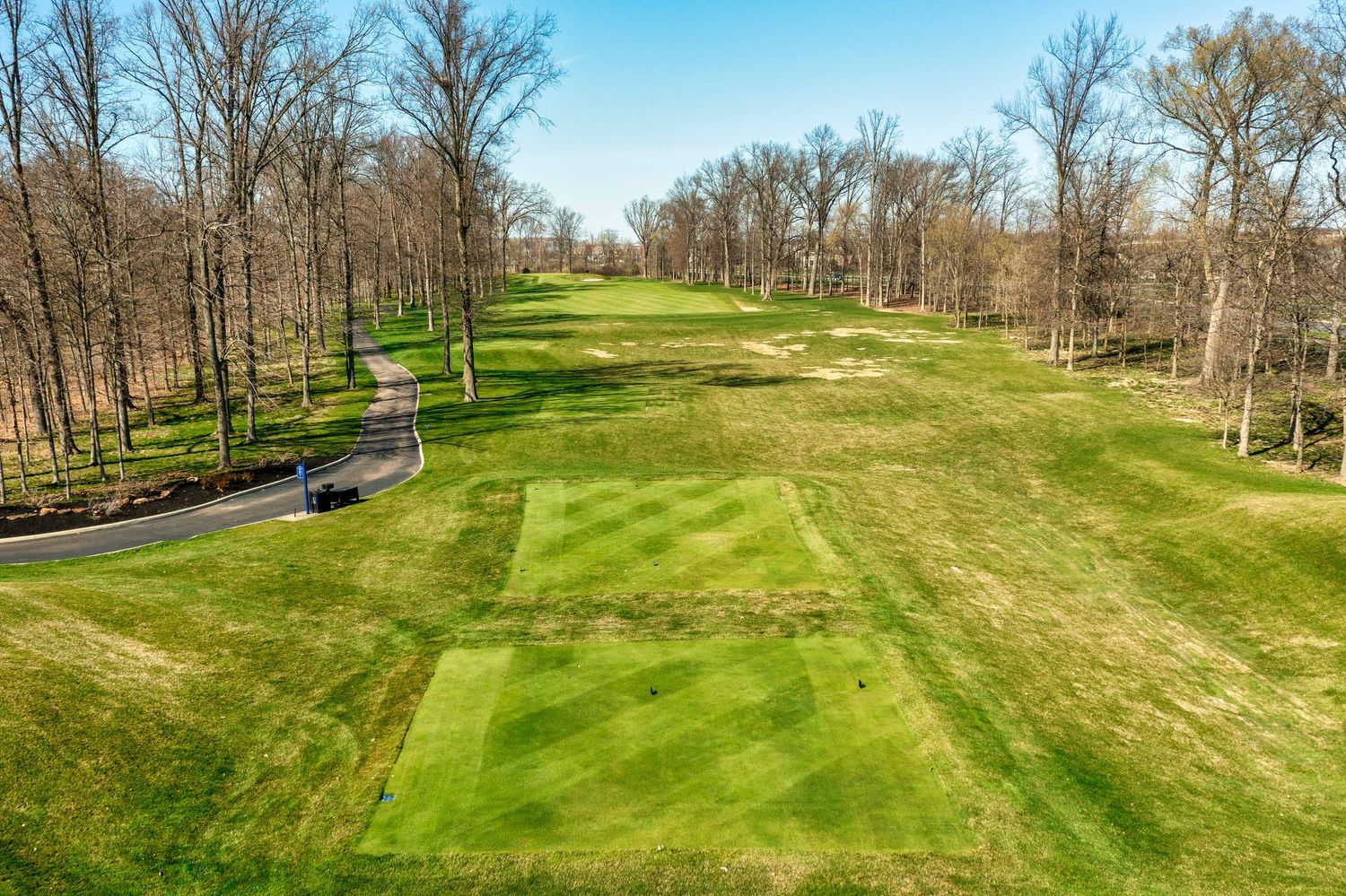 Aerial view of a scenic golf course fairway with lush green grass surrounded by bare trees in early spring.