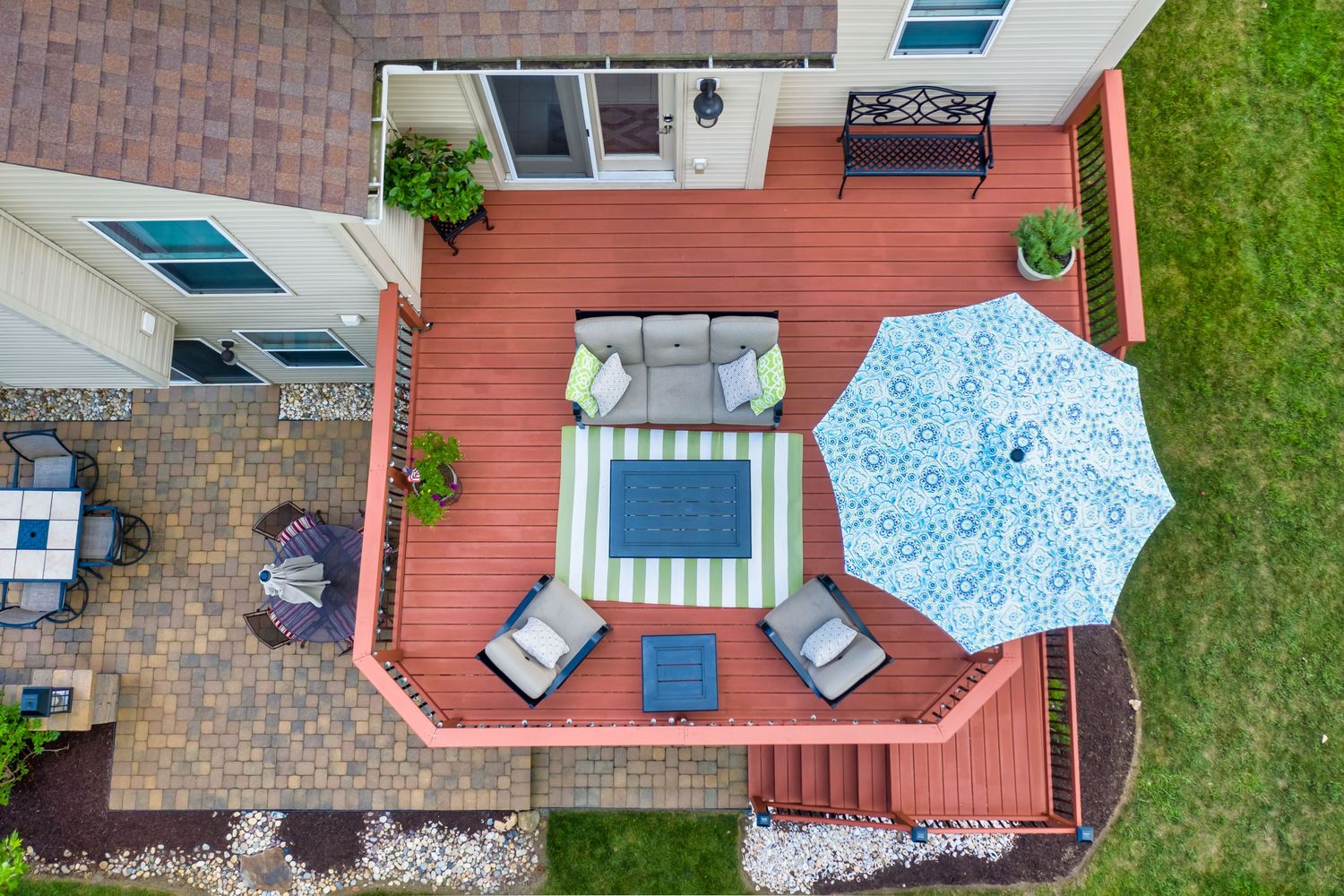 Aerial drone view of a backyard deck with comfortable patio furniture and a large blue and white striped umbrella for a real estate listing.