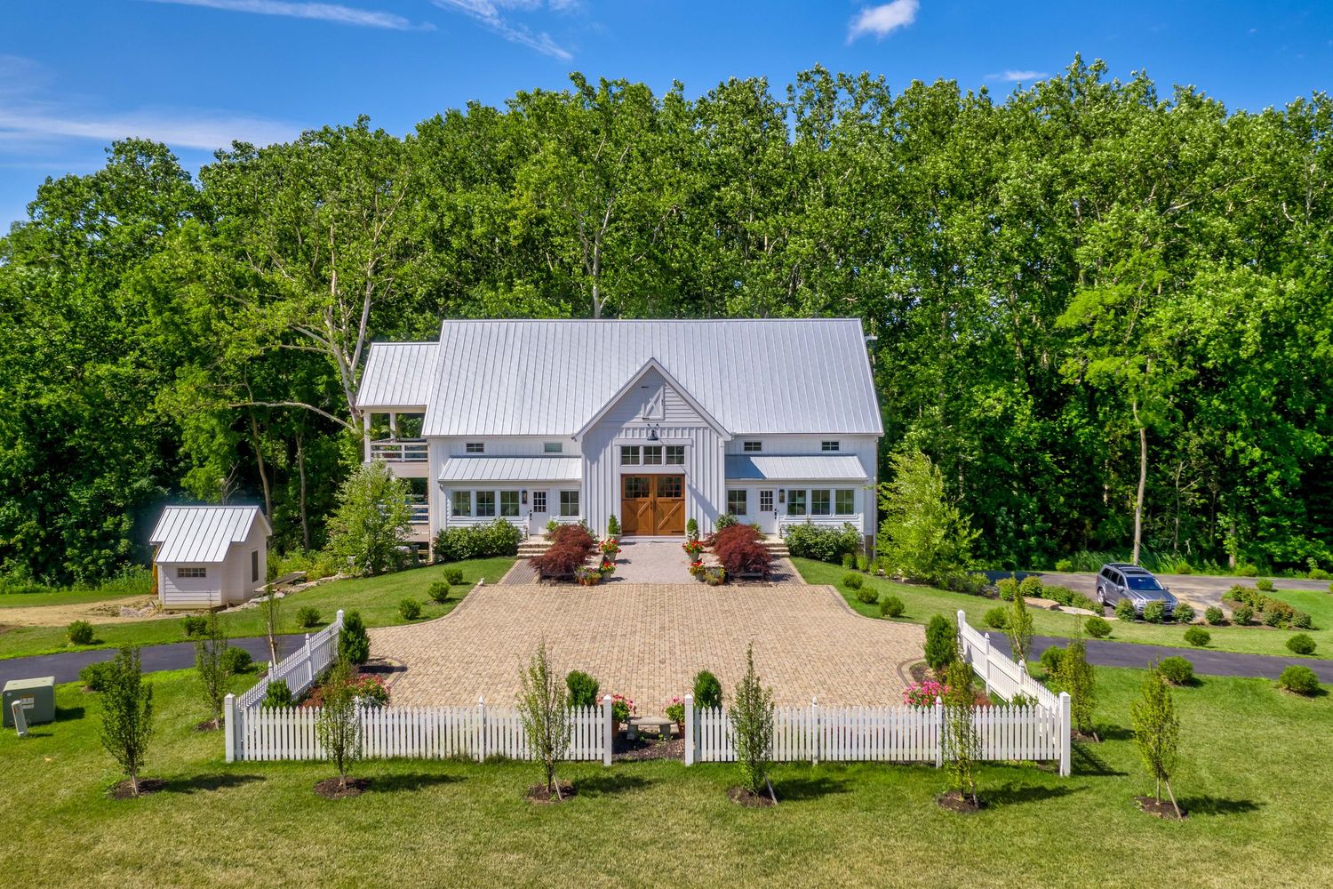 Modern farmhouse with white picket fence and metal roof nestled among green trees on manicured property in Powell, Ohio.