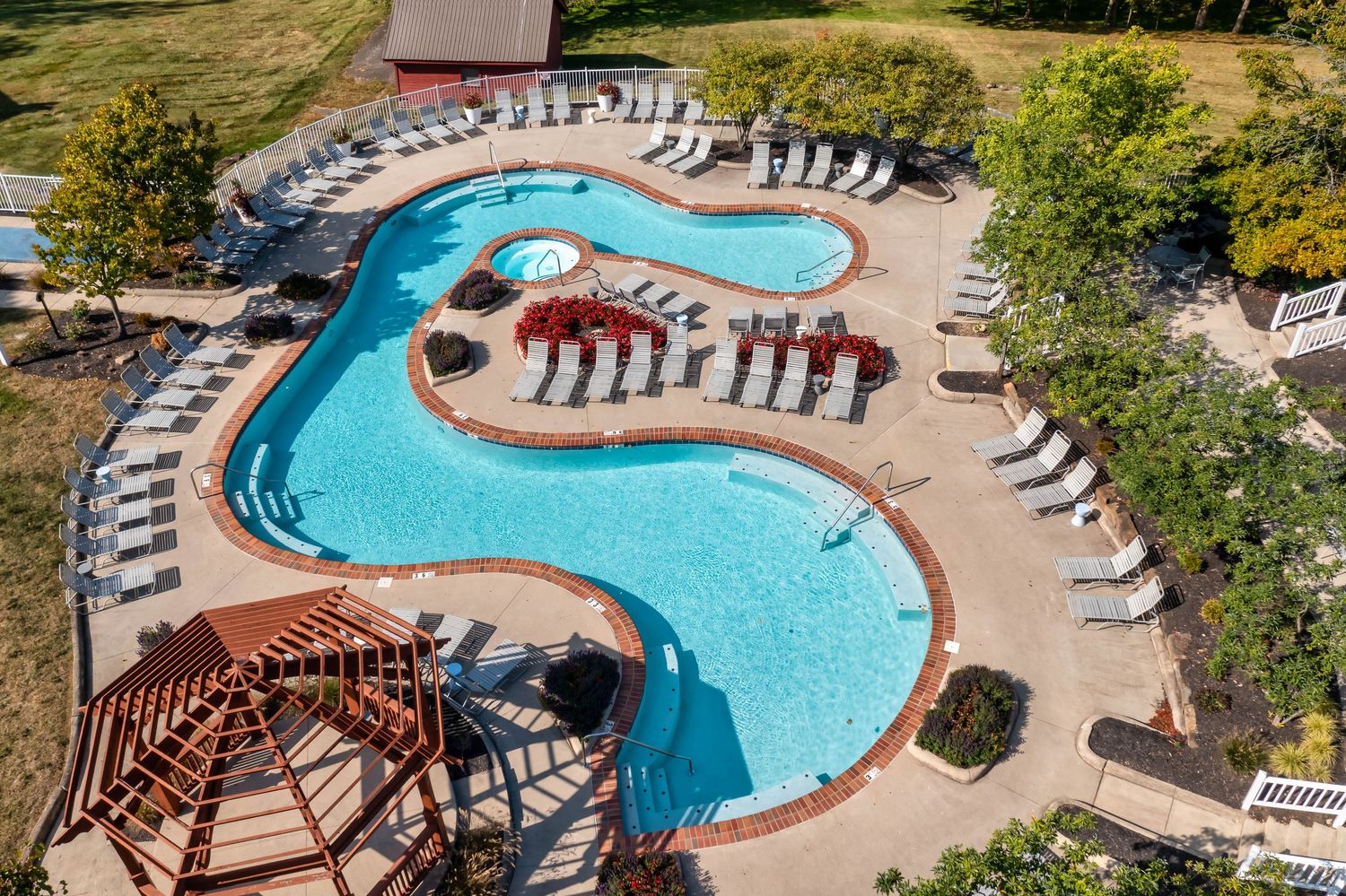 Aerial view of a curved swimming pool with brown pergolas and lounge chairs at a luxury resort multi-family apartment property.