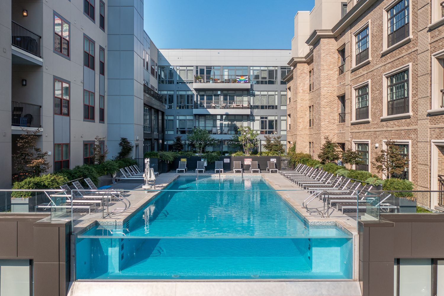 Modern apartment complex features a luxurious outdoor pool area with lounge chairs surrounded by contemporary architecture.
