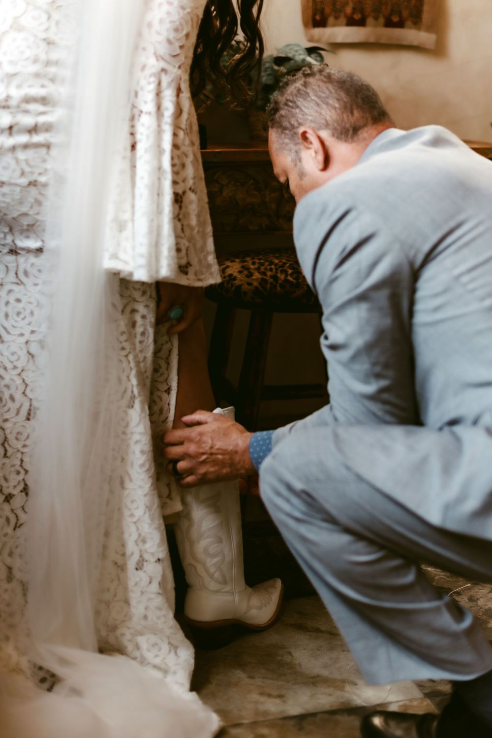 Person in gray suit adjusts white wedding dress train.