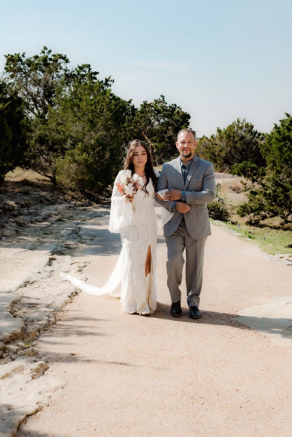 A couple walks along a path outdoors during their wedding day ceremony.
