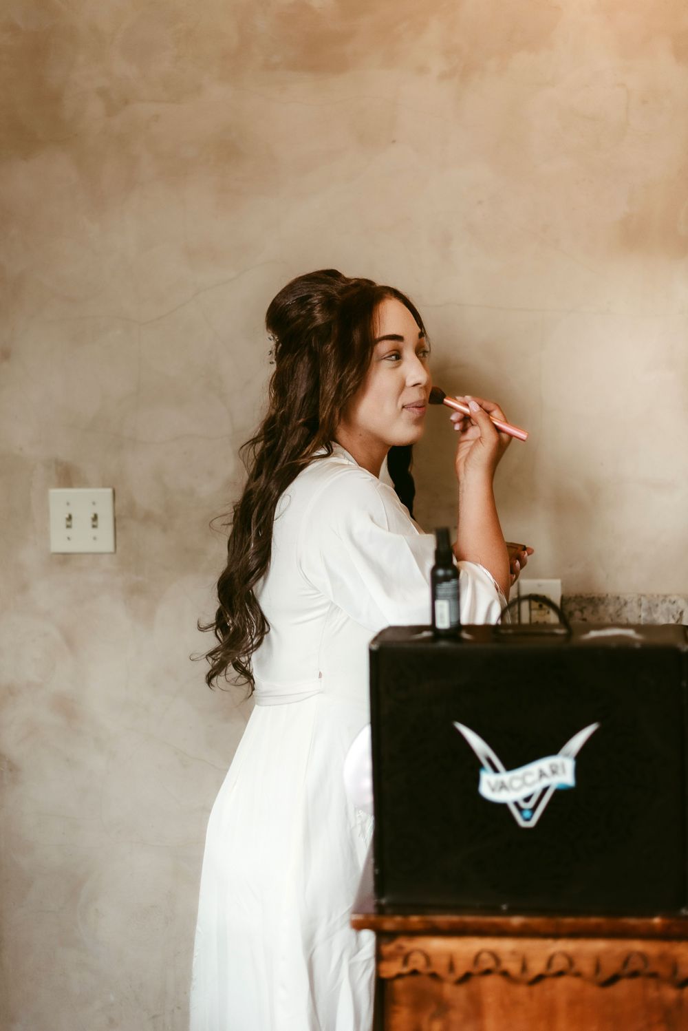 A woman in white applies makeup in front of a vintage-style makeup case.