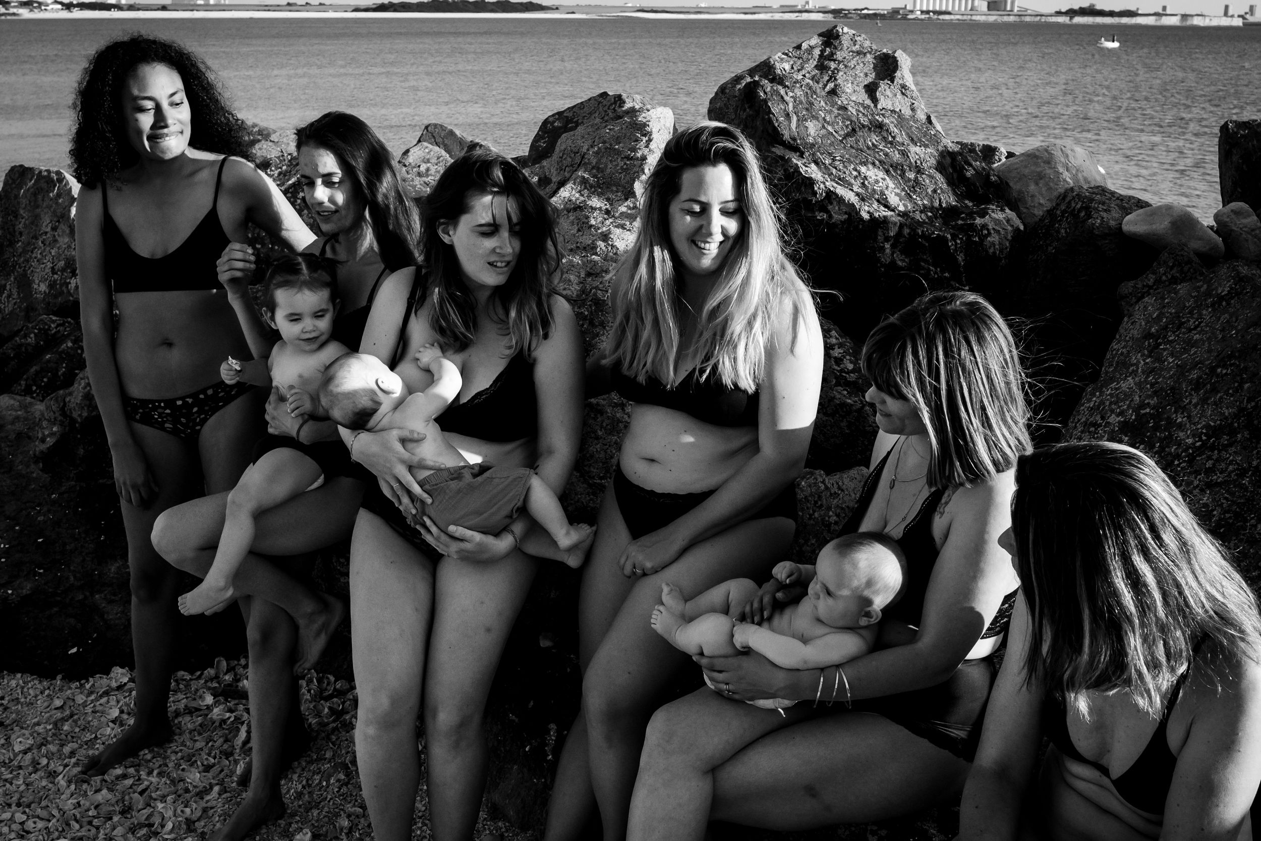 A group of friends in swimwear relaxing together on rocky beach in black and white photography.