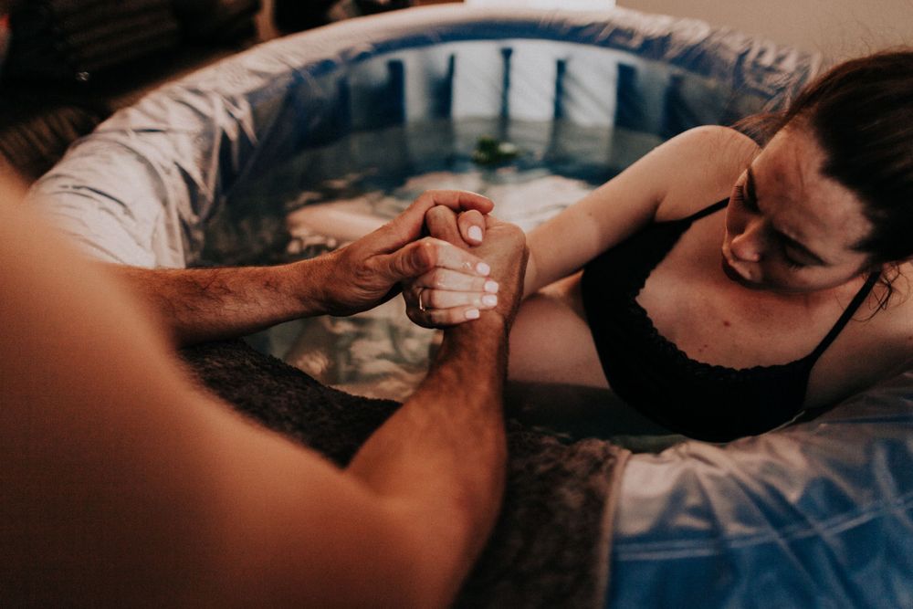 mother holding partners hand as she labours in the birthing pool at home