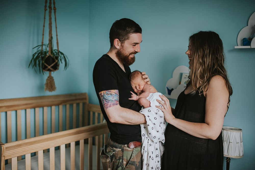 Tattooed father holds newborn son with his wife, the child is giving metal hand sign for rock on.